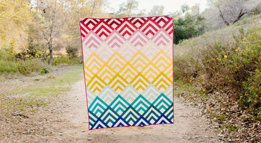 Modern geometric quilt by Cotton and Joy with layered chevron blocks in warm and cool tones