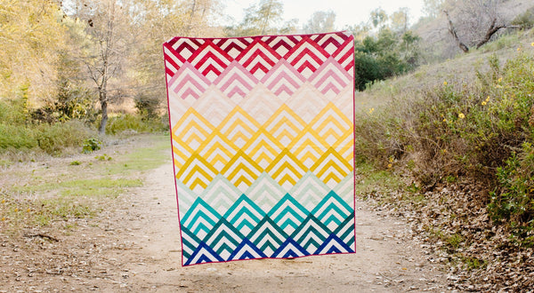 Modern geometric quilt by Cotton and Joy with layered chevron blocks in warm and cool tones