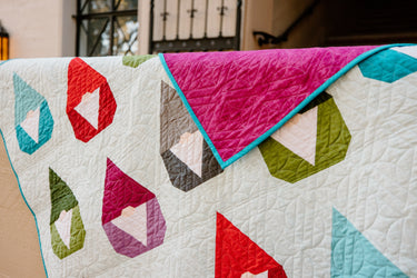 Vibrant Nordic Gnome quilt by Cotton and Joy, draped to reveal contrasting magenta backing, showcasing modern quilt pattern design.