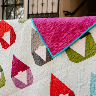 Vibrant Nordic Gnome quilt by Cotton and Joy, draped to reveal contrasting magenta backing, showcasing modern quilt pattern design.